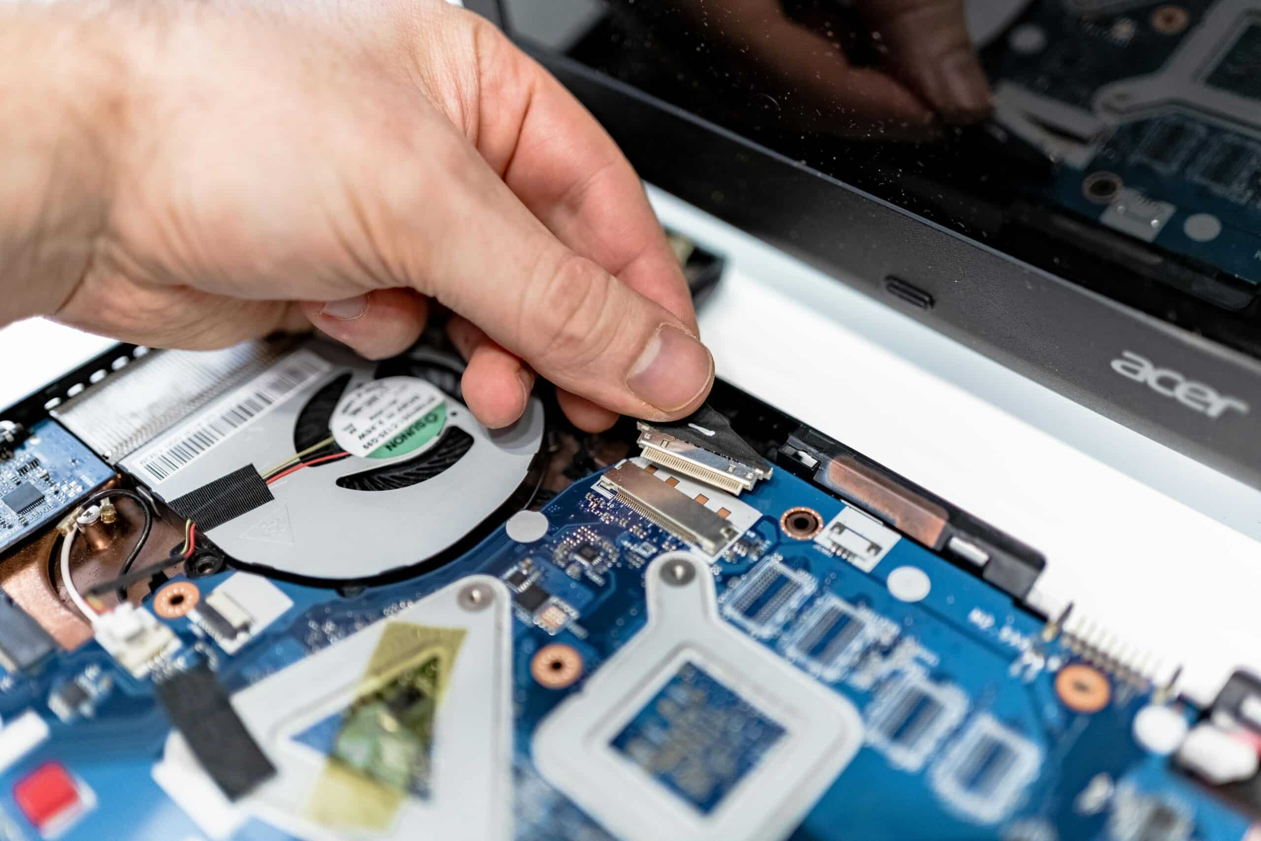 A hand connects parts on a laptop motherboard, showing intricate electronic components.